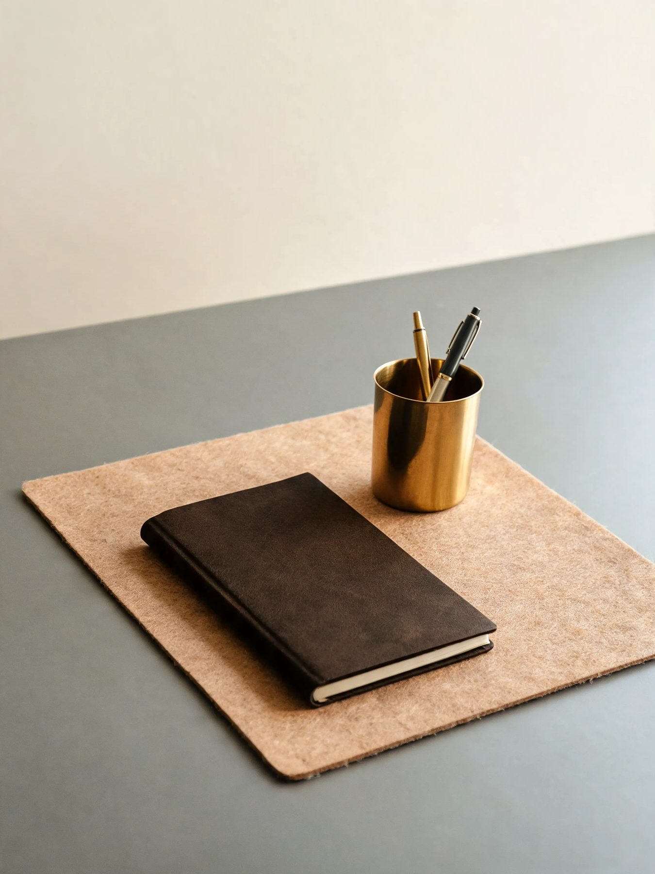 Walnut desk shelf with a felt mat and a brass pen cup on a matte grey desk